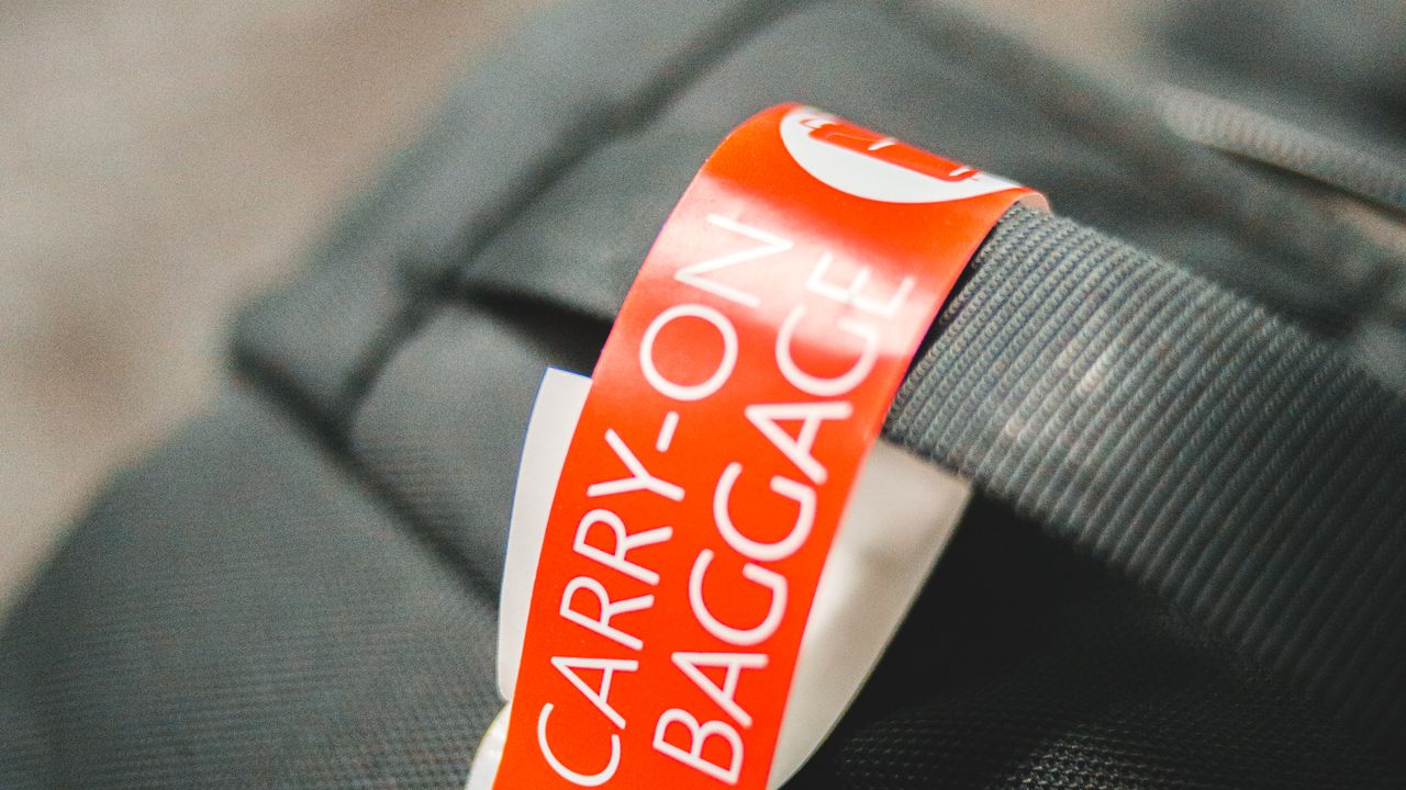 A printed carry-on baggage tag looped around the handle strap of a travel bag